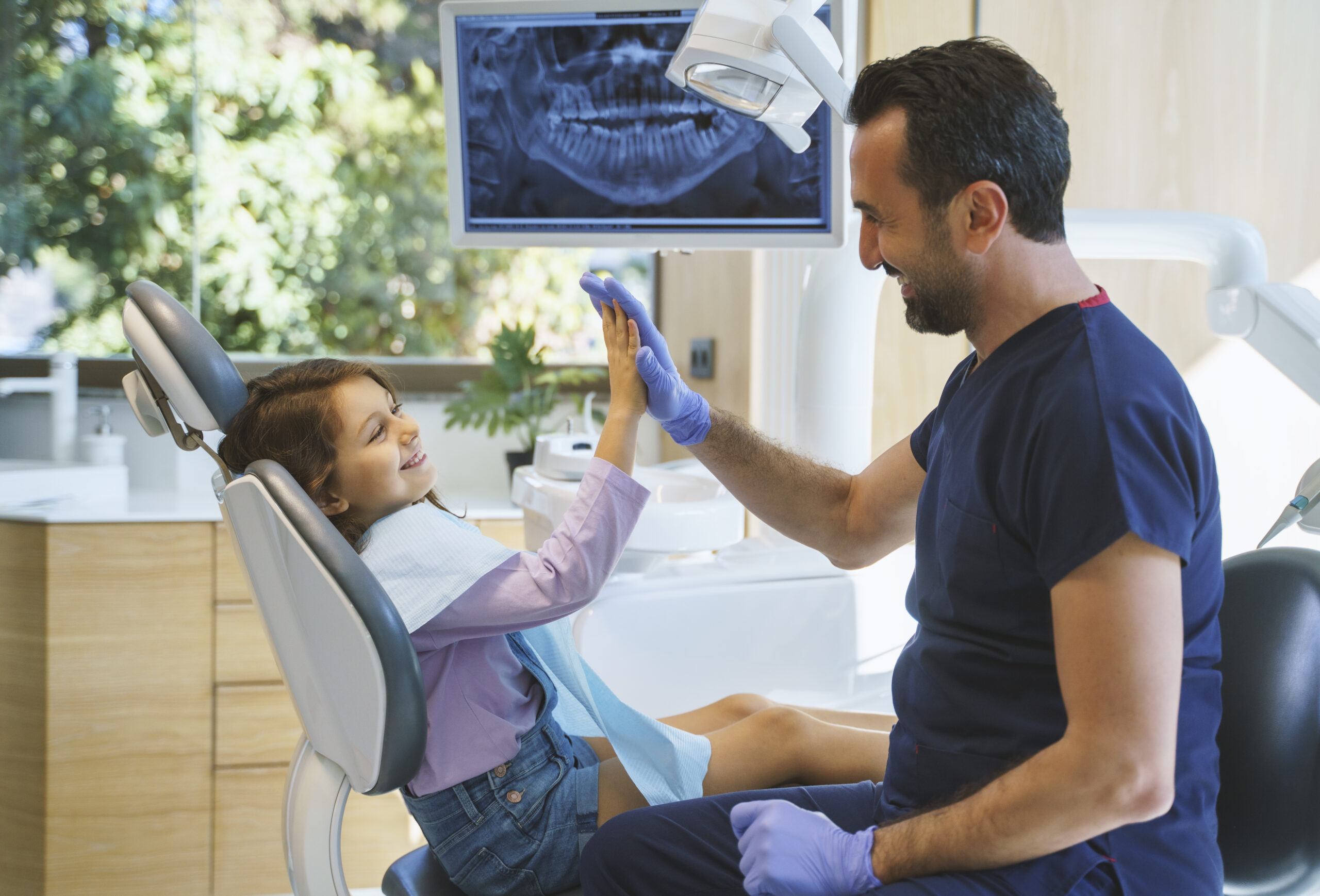 Close up portrait of a male dentist giving a high five to little girl at dental clinic